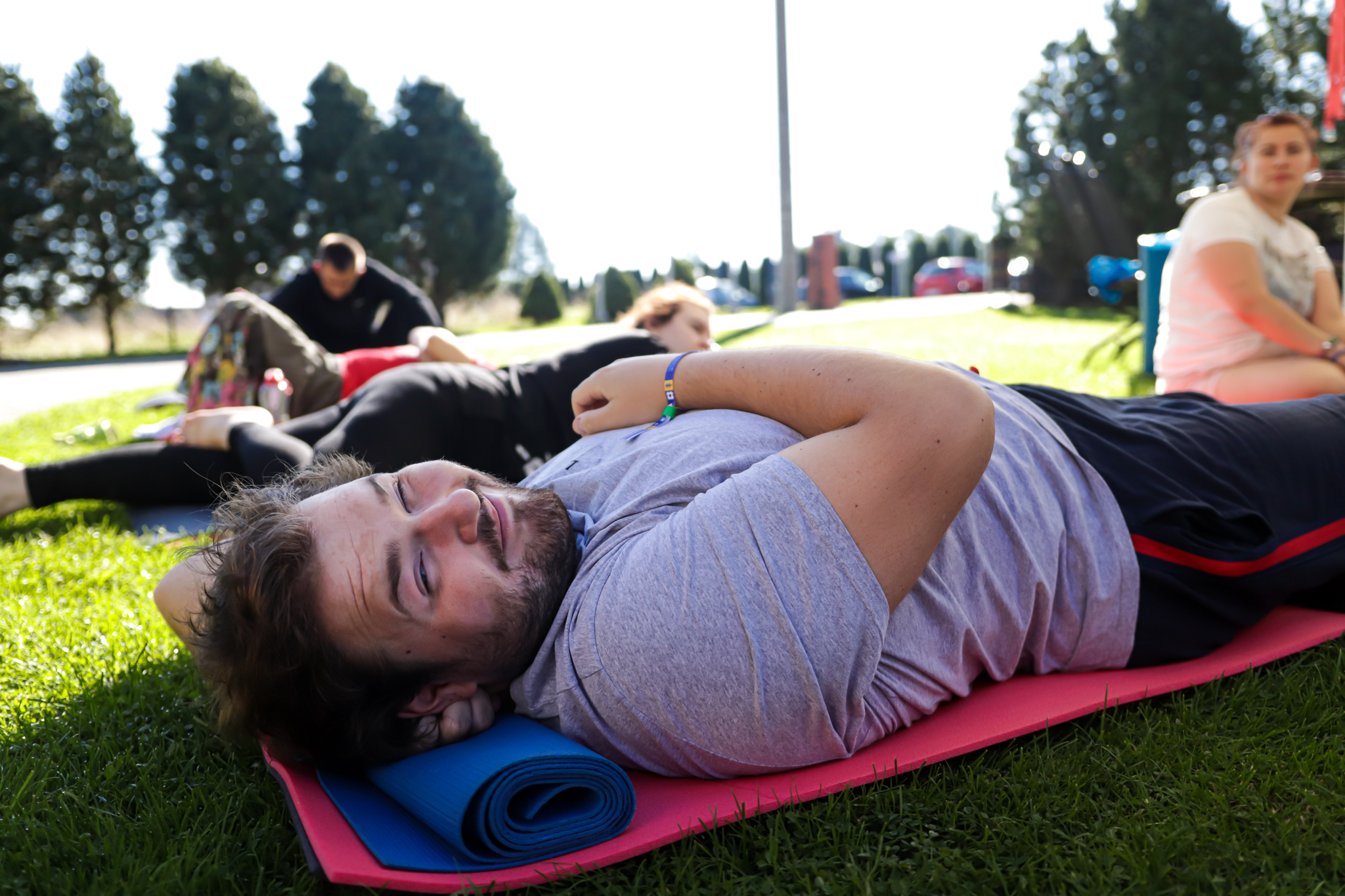 Młody, uśmiechnięty mężczyzna leżący na macie do ćwiczeń na zewnątrz.