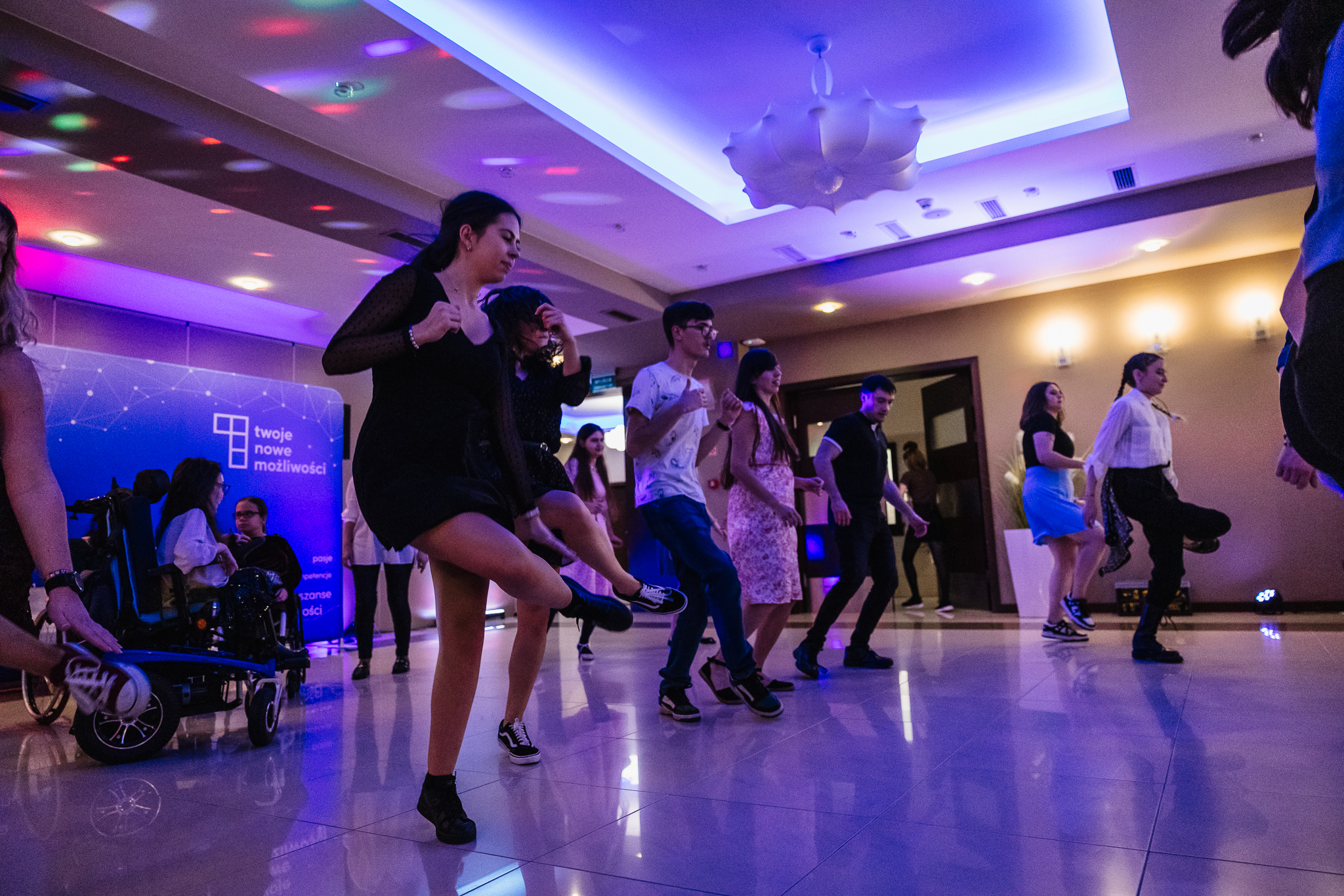 Grupa osób ustawiona w szeregu i tańcząca ułożony układ taneczny.