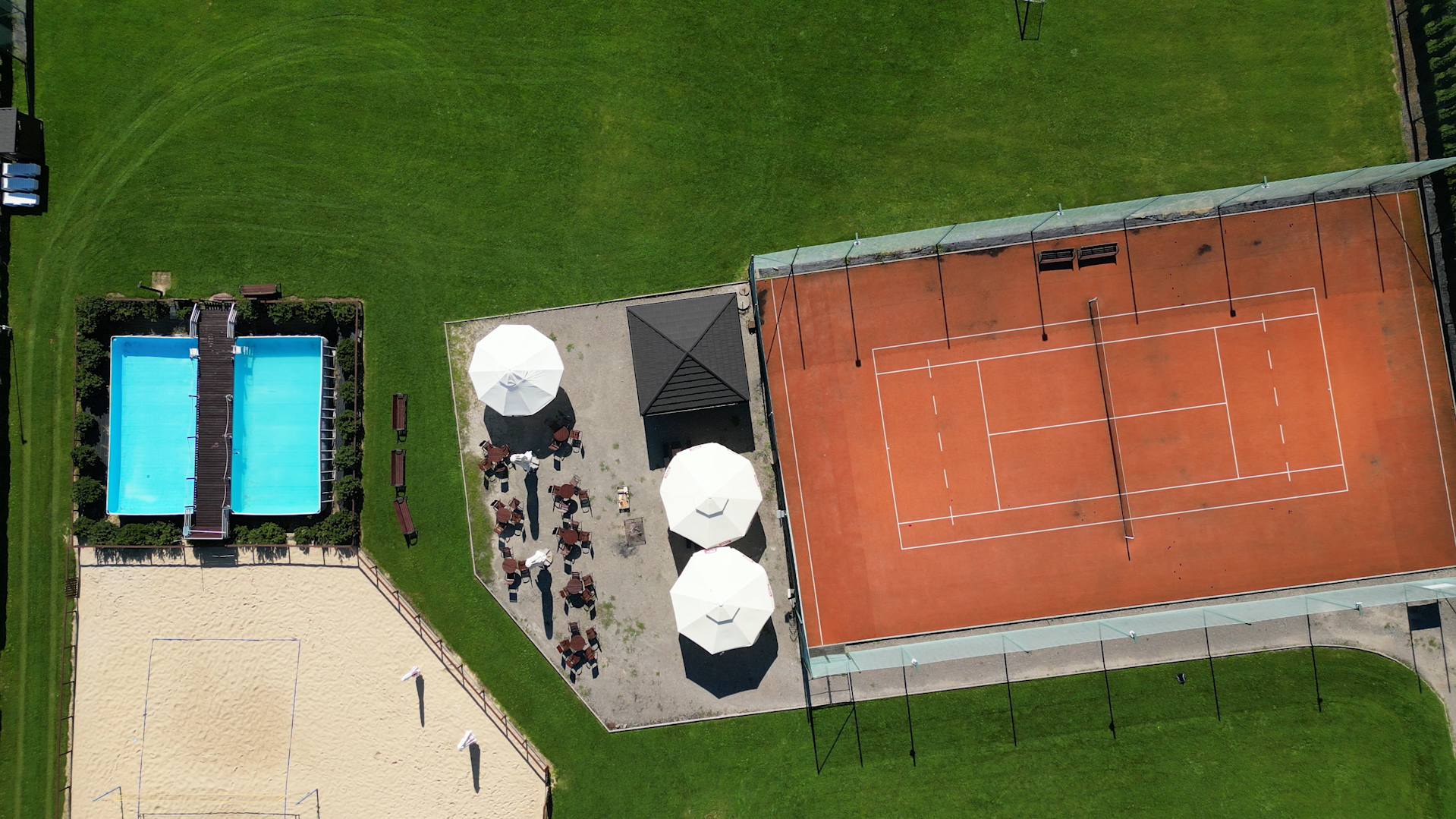 Widok z lotu ptaka na kort tenisowy, baseny zewnętrzne, boisko do piłki plażowej oraz przestrzeń relaksacyjną.